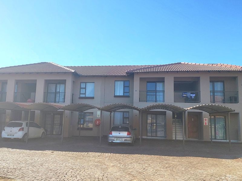 Front elevation of a multi-story apartment complex featuring covered parking bays, balconies, and paved driveway access.