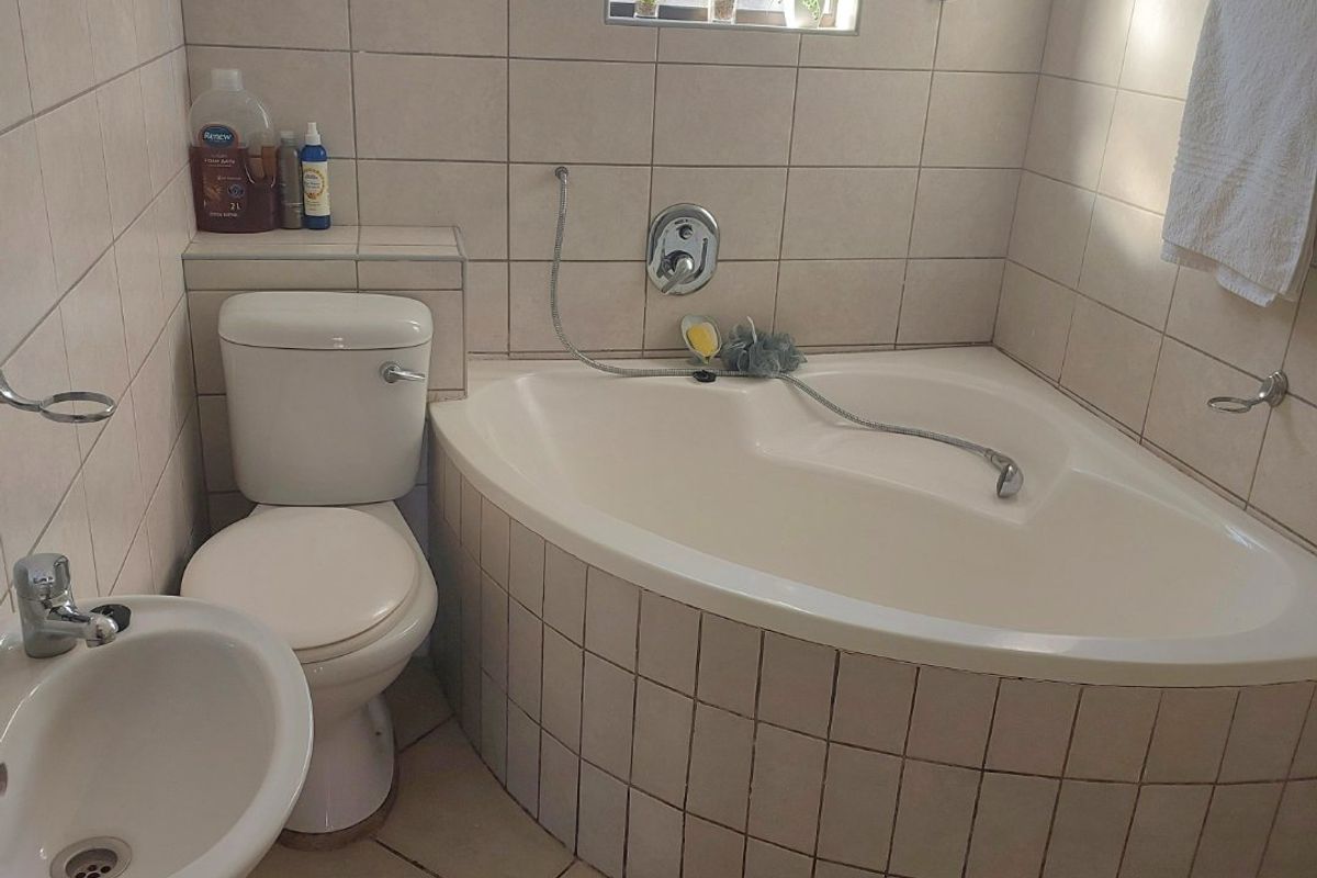 A functional bathroom featuring a corner bathtub, pedestal basin, and toilet with neutral wall and floor tiling.