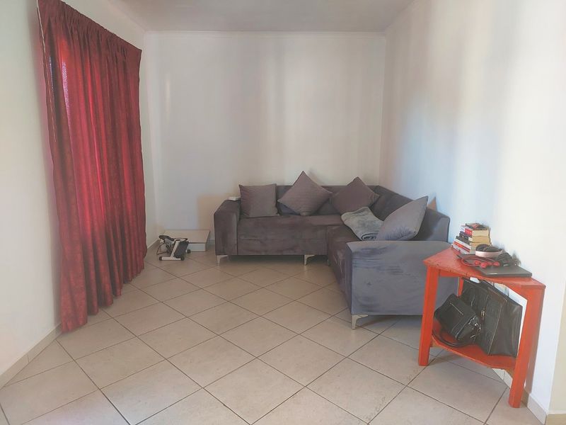 A living room area featuring neutral tiled flooring and plain white walls, providing a simple and functional space.