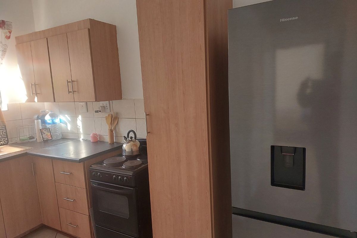 A functional kitchen featuring light wood-finish cabinetry, dark countertops, tiled backsplash, and a dedicated tall pantry cupboard for additional storage.