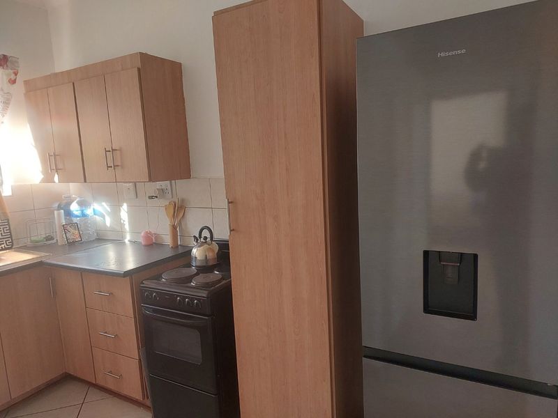 A functional kitchen featuring light wood-finish cabinetry, dark countertops, tiled backsplash, and a dedicated tall pantry cupboard for additional storage.