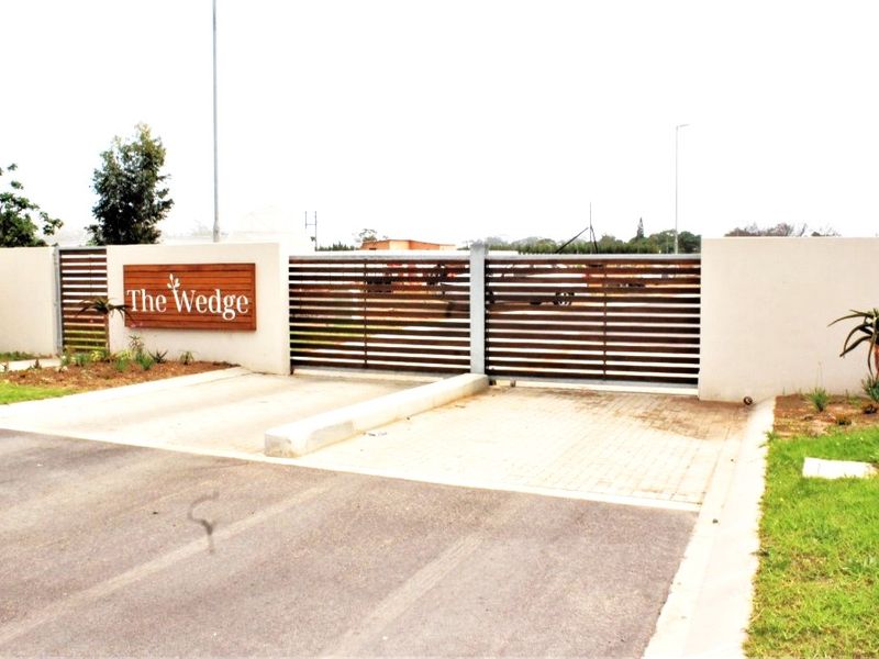 The entrance to The Wedge complex featuring a modern horizontal slat sliding gate, perimeter walling, and paved driveway access.