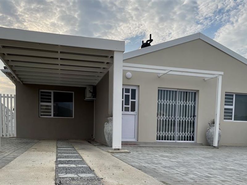 Front elevation of a townhouse featuring a paved driveway, covered carport, and secure sliding door entrance.