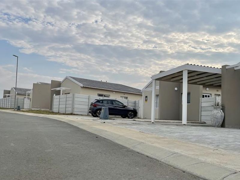 A street-level view of a modern townhouse complex featuring paved driveways, covered carports, and neat precast boundary walls under a cloudy sky.