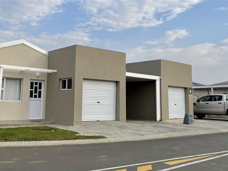 Front elevation of a modern townhouse featuring a paved driveway, single garage, and an additional carport area.