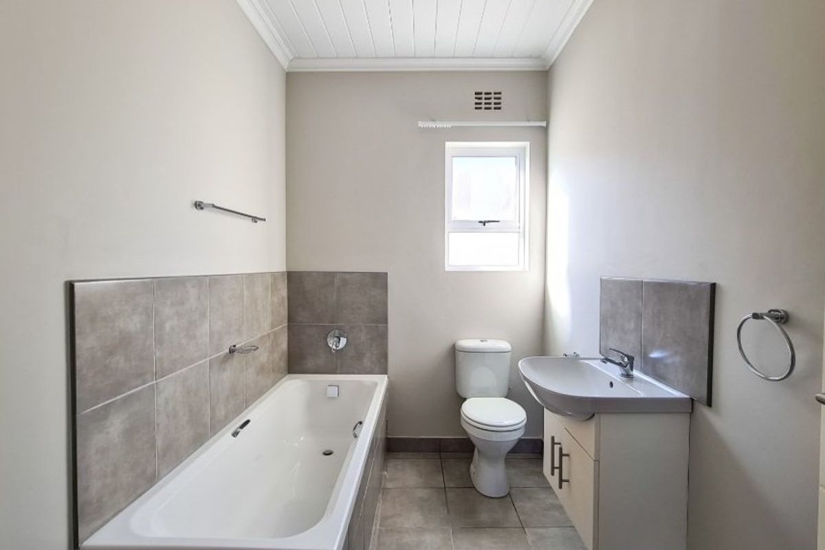 A clean and well-maintained bathroom featuring a bathtub, a modern vanity with a washbasin, and neutral wall and floor tiling.