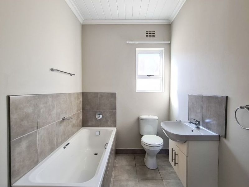 A clean and well-maintained bathroom featuring a bathtub, a modern vanity with a washbasin, and neutral wall and floor tiling.