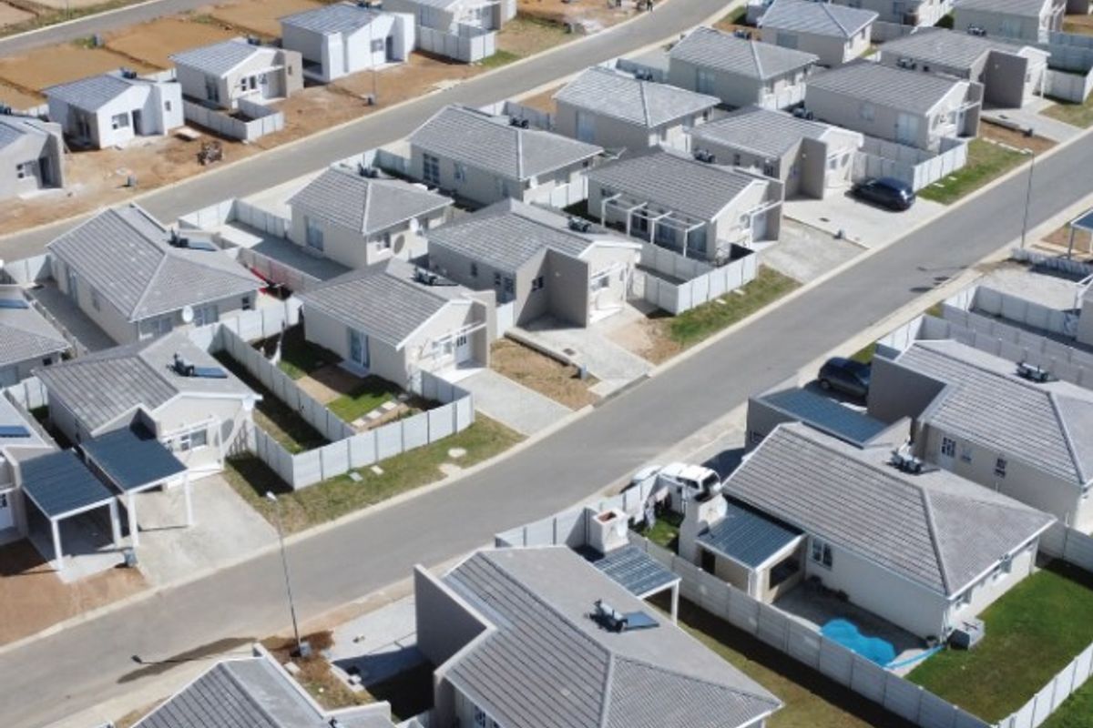 An aerial view of a modern residential townhouse development featuring uniform tiled roof homes, paved driveways, and established boundary fencing.
