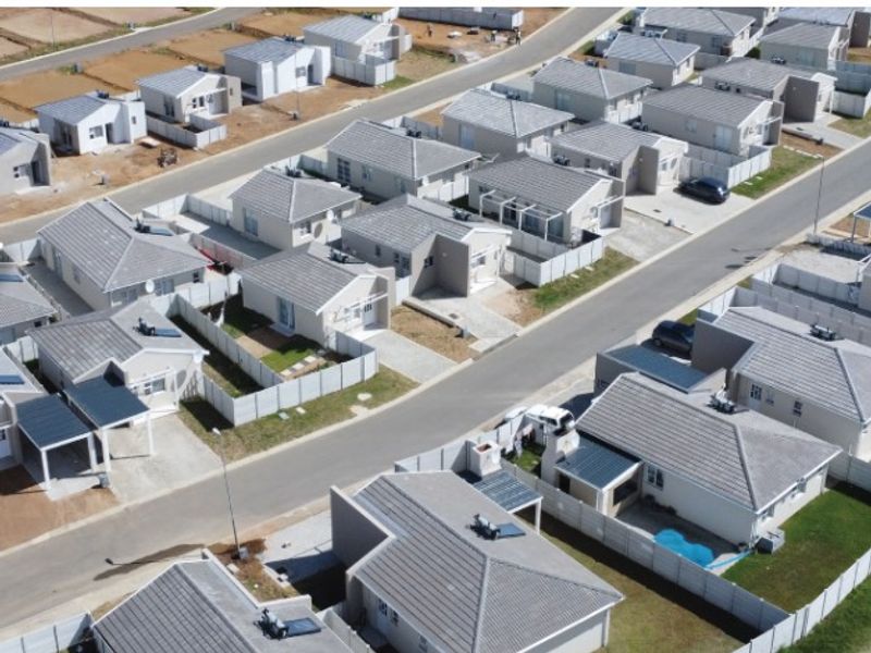 An aerial view of a modern residential townhouse development featuring uniform tiled roof homes, paved driveways, and established boundary fencing.