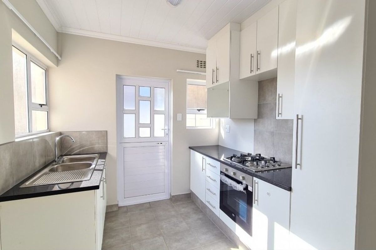 A clean, modern kitchen featuring white cabinetry, dark countertops, a gas hob, built-in oven, and direct access to the exterior.