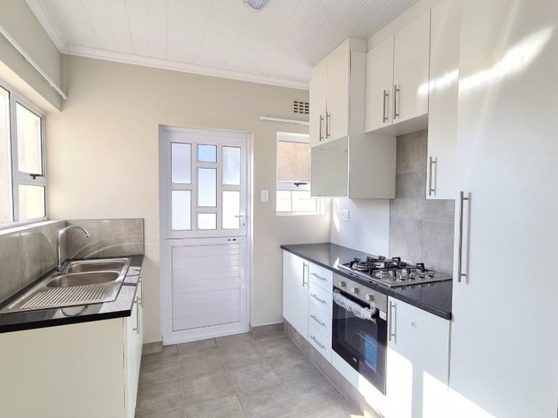 A clean, modern kitchen featuring white cabinetry, dark countertops, a gas hob, built-in oven, and direct access to the exterior.