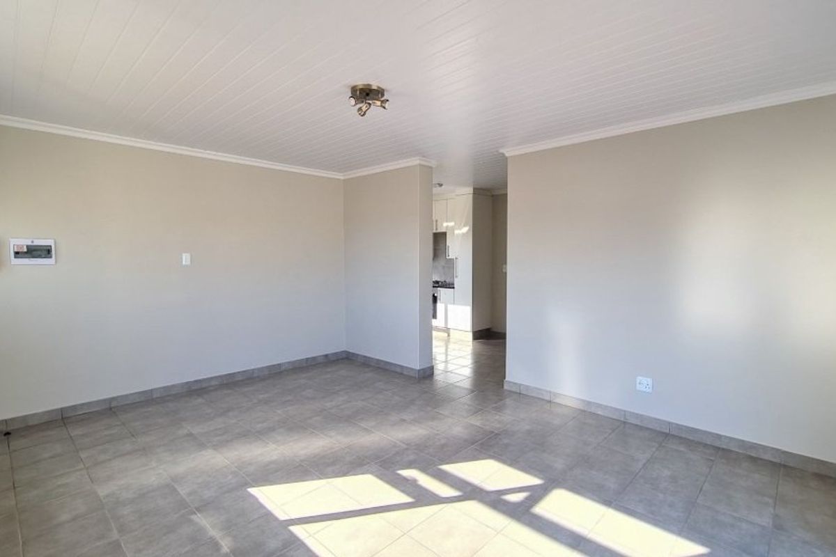 Spacious open-plan living area featuring neutral tiled flooring and a clean tongue and groove ceiling, with a clear view into the adjacent kitchen.