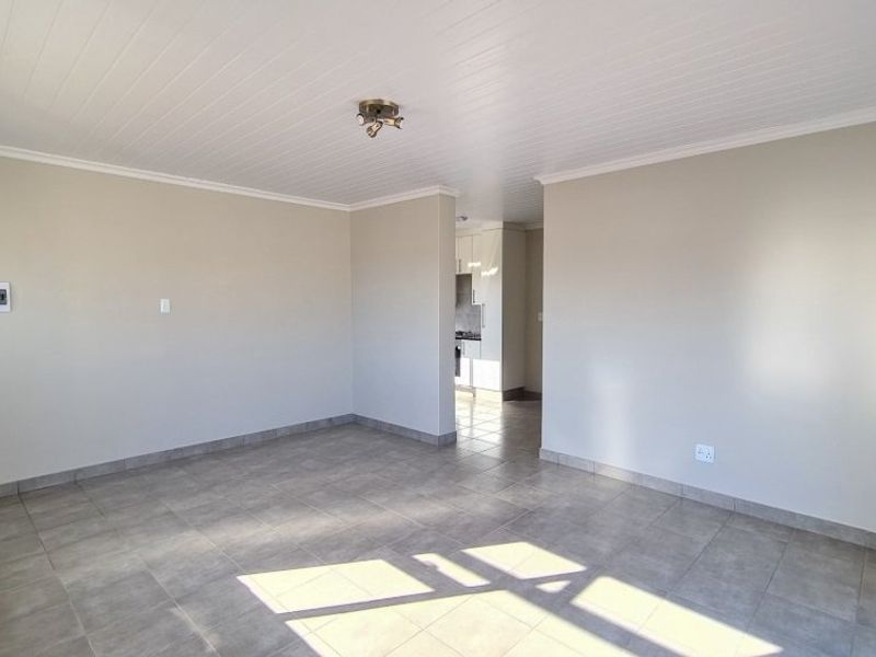 Spacious open-plan living area featuring neutral tiled flooring and a clean tongue and groove ceiling, with a clear view into the adjacent kitchen.