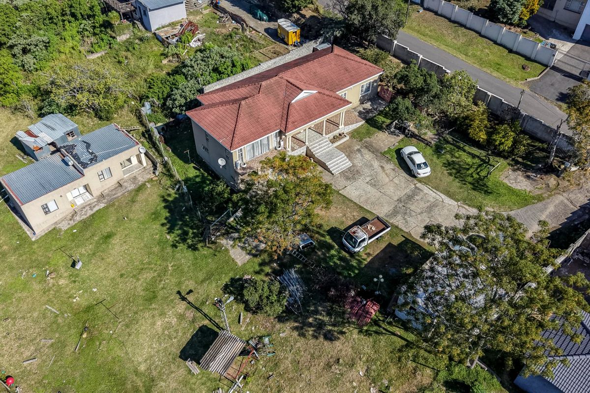 Aerial view of a residential property featuring a main house with a tiled roof, concrete driveway, and a separate outbuilding on a large plot.