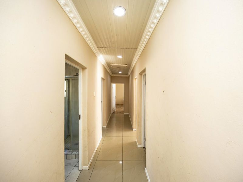 A long, empty hallway featuring tiled flooring, a panelled ceiling with decorative cornice, and recessed downlighting, providing access to multiple rooms.