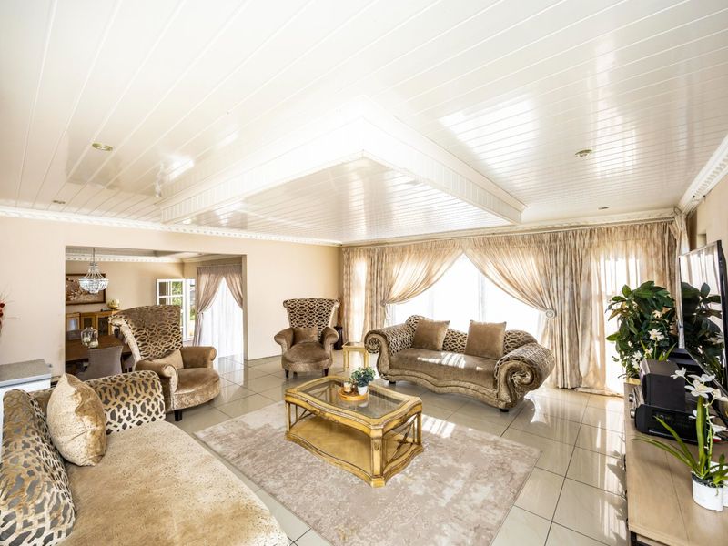 Spacious open-plan living area featuring glossy tiled flooring, a distinctive coffered ceiling with recessed lighting, and elegant crown molding throughout.