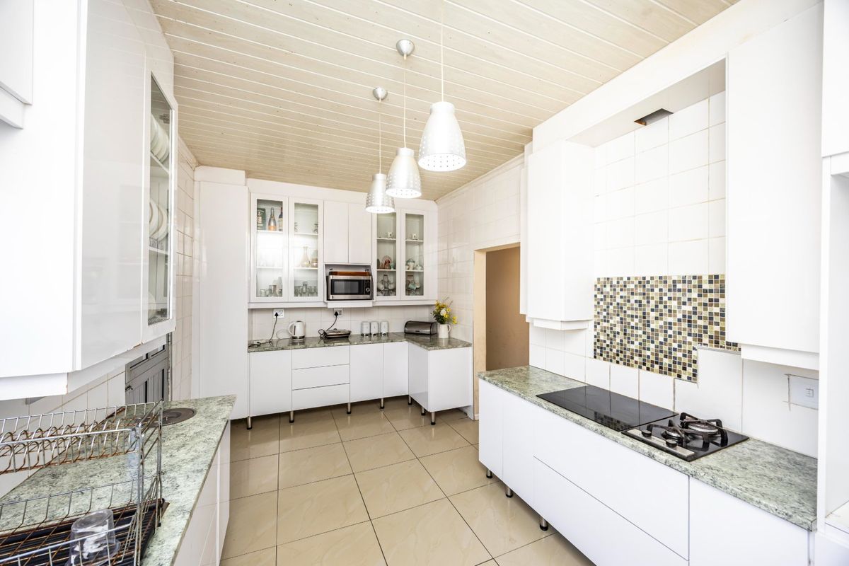 A bright, functional kitchen featuring white cabinetry, stone countertops, integrated hob, built-in microwave, and a distinctive timber ceiling with pendant lighting.