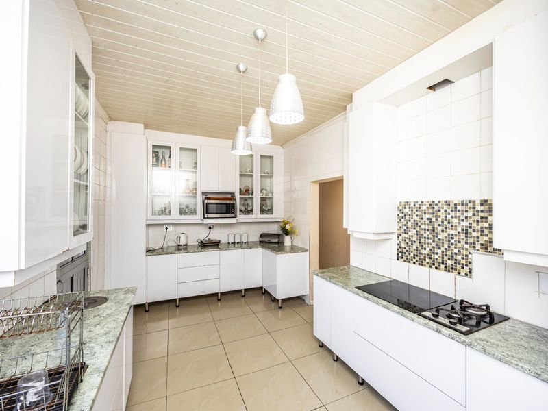 A bright, functional kitchen featuring white cabinetry, stone countertops, integrated hob, built-in microwave, and a distinctive timber ceiling with pendant lighting.