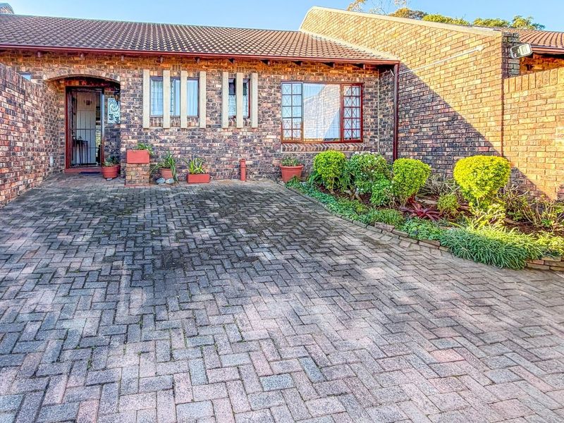 Front view of a brick townhouse featuring a paved driveway, secure entrance, and established garden beds.