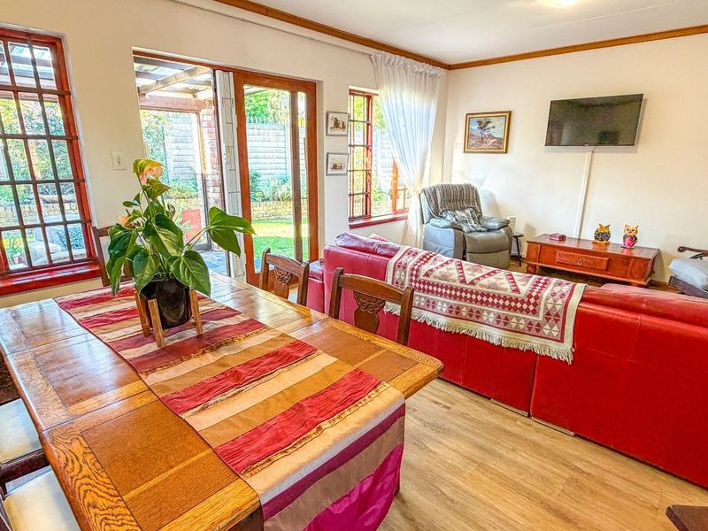 Open-plan living and dining area featuring laminate flooring, timber-framed windows, and sliding doors providing direct access to the outdoor patio area.