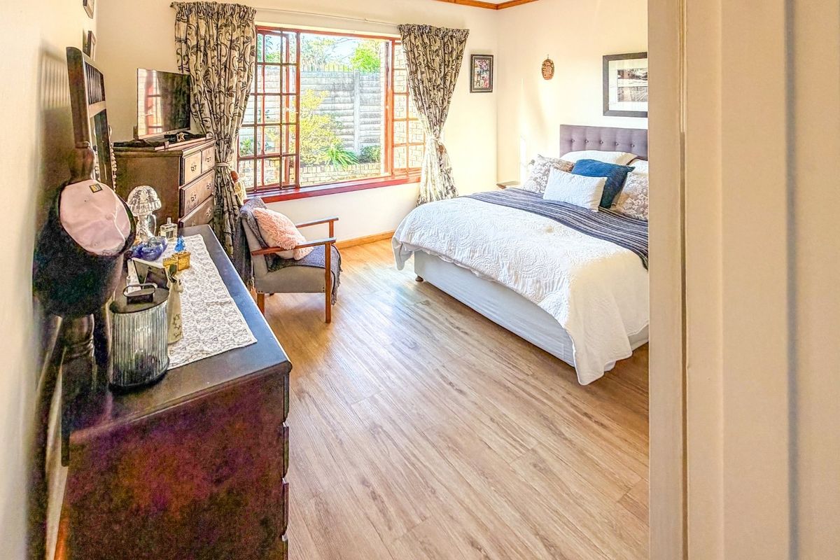 A well-lit bedroom featuring laminate flooring and a large timber-framed window overlooking the garden area.