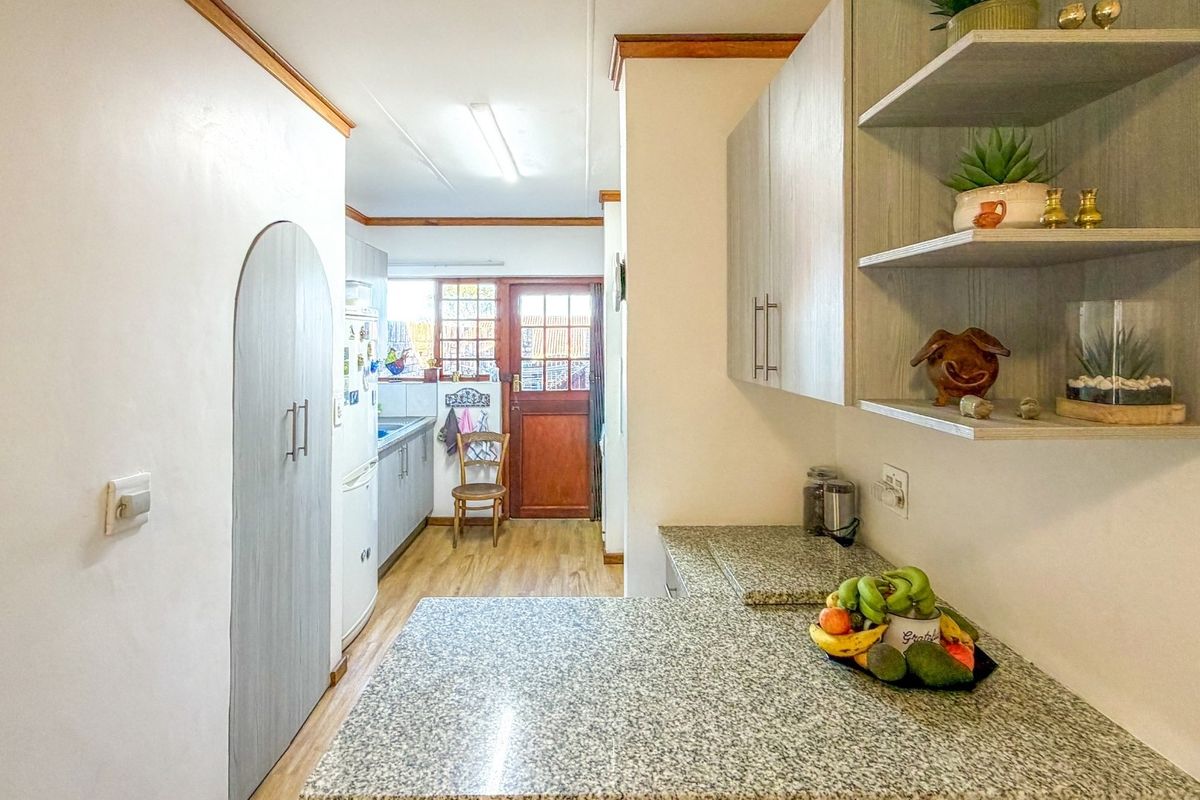 A functional kitchen featuring granite countertops, built-in cabinetry, and open shelving, leading through to a rear access door with timber detailing.