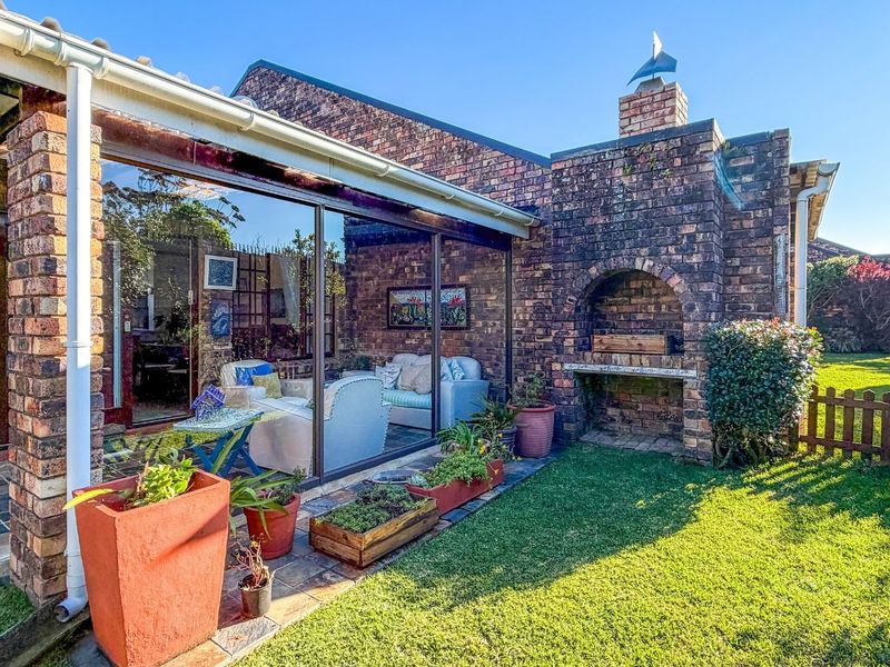 A covered brick patio featuring a built-in fireplace and braai area, with large sliding glass doors leading into the home and a private garden.