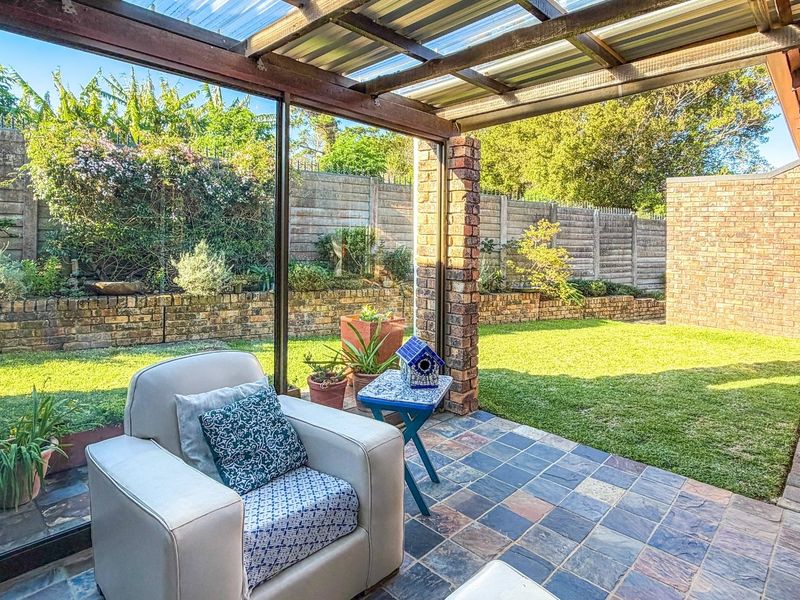 A covered patio area featuring slate tile flooring and brick pillars, overlooking a private garden with a brick boundary wall.