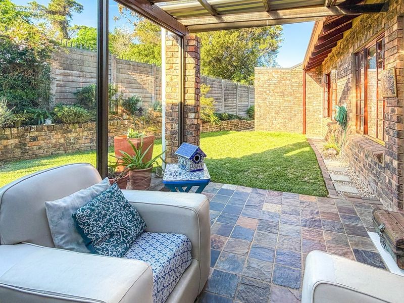A covered patio area featuring slate tile flooring, brick walls, and direct access to a private garden space.