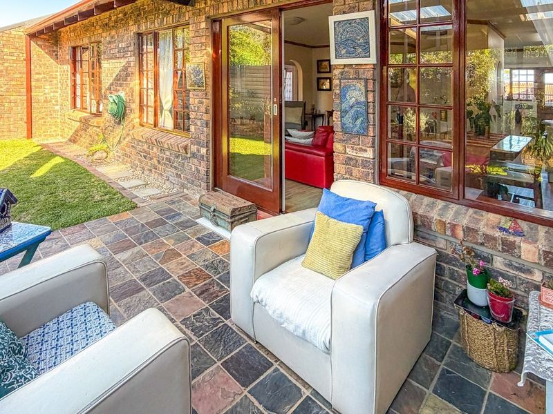 A covered patio area featuring slate tile flooring and exposed brick walls, providing direct access to the interior living space through timber frame sliding doors.