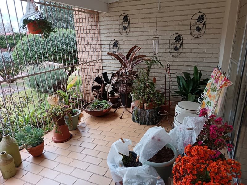A covered patio area featuring brick flooring and a painted brick wall, enclosed by metal security bars, offering a functional outdoor space.