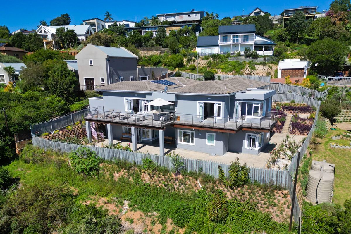 Aerial view of a multi-level residential property featuring a raised deck, paved patio area, solar panels, and landscaped terraced garden.