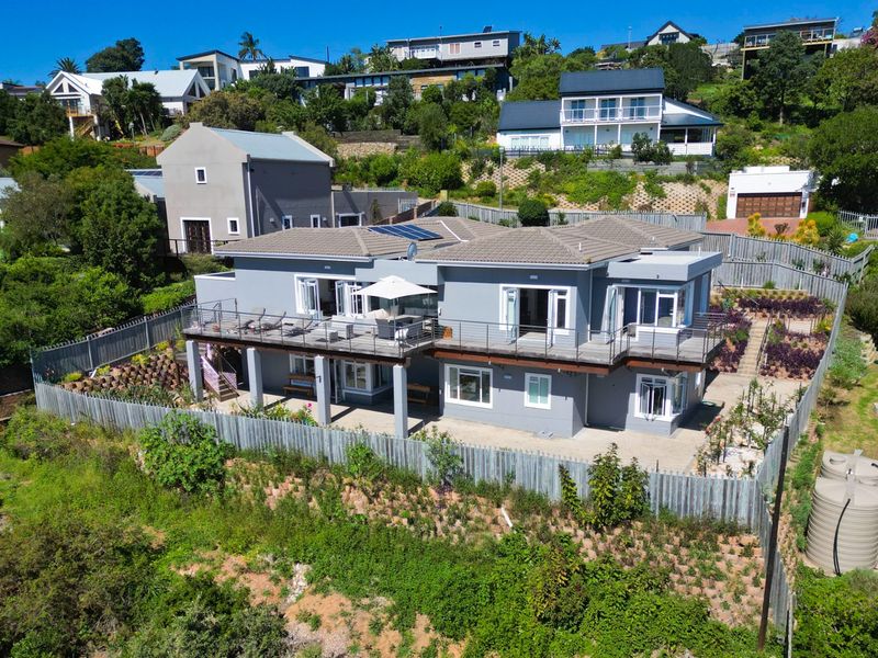 Aerial view of a multi-level residential property featuring a raised deck, paved patio area, solar panels, and landscaped terraced garden.