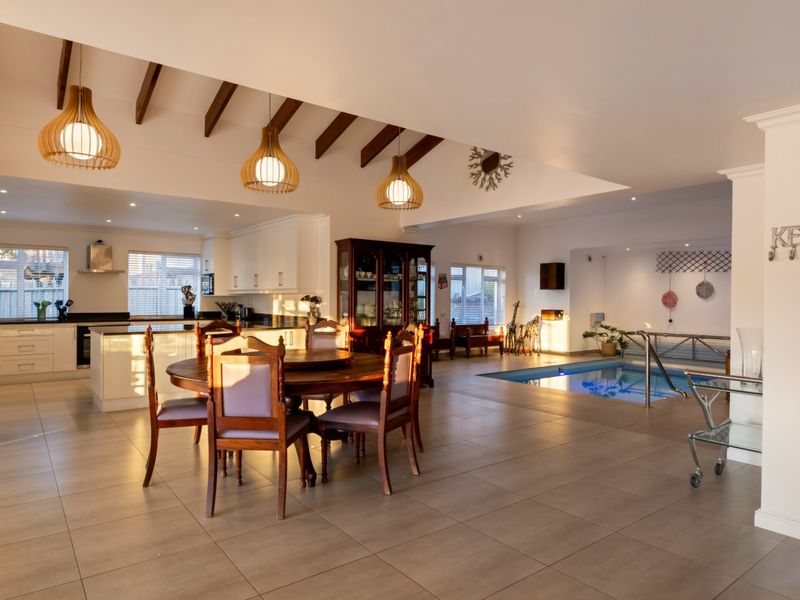 Spacious open-plan living area featuring exposed timber beams, a modern kitchen with island, and a unique integrated indoor swimming pool.