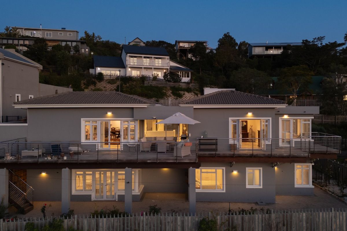 An elevated rear view of the property featuring a spacious timber deck with stainless steel balustrades, paved patio area, and multiple access points.