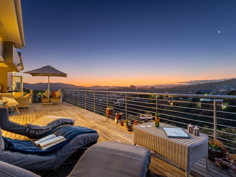 Spacious elevated timber balcony featuring a stainless steel balustrade and panoramic sunset views over the surrounding landscape.