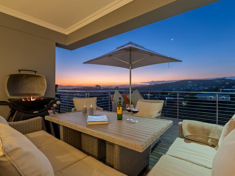 A covered balcony featuring timber decking and a stainless steel balustrade, offering expansive sunset views over the surrounding landscape.