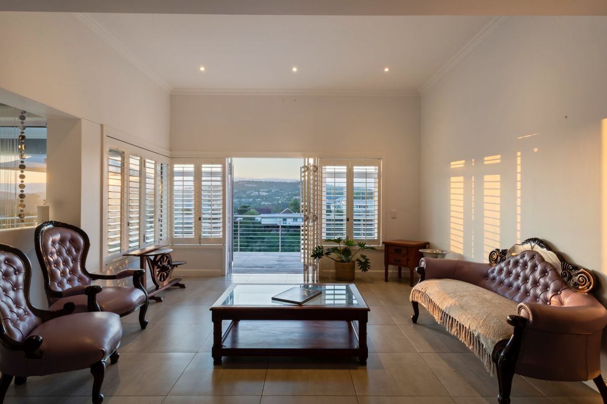 Spacious living room featuring tiled flooring, recessed lighting, and plantation shutters, with bi-fold doors opening to a balcony with scenic views.