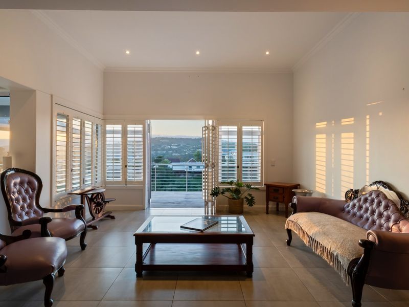 Spacious living room featuring tiled flooring, recessed lighting, and plantation shutters, with bi-fold doors opening to a balcony with scenic views.