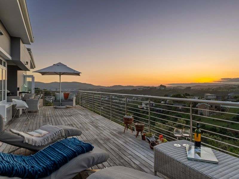 Spacious elevated timber deck balcony featuring a stainless steel balustrade and panoramic sunset views over the surrounding landscape.