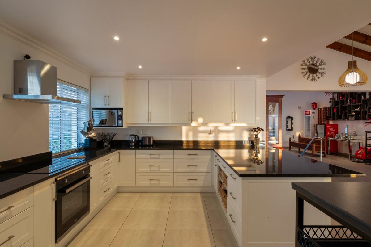 Modern kitchen featuring white cabinetry, black granite countertops, built-in oven, extractor fan, and tiled flooring with recessed lighting.