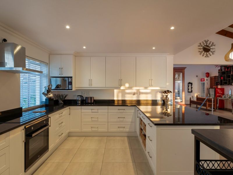 Modern kitchen featuring white cabinetry, black granite countertops, built-in oven, extractor fan, and tiled flooring with recessed lighting.