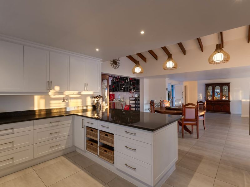 Spacious open-plan kitchen and dining area featuring modern white cabinetry, granite countertops, exposed timber ceiling beams, and contemporary pendant lighting.