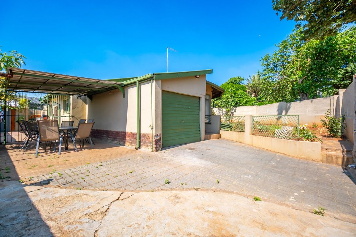 Rear exterior view featuring a single garage, paved driveway, and a covered patio area with boundary walling.
