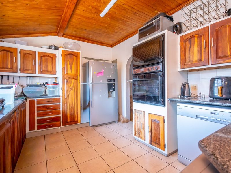 A functional kitchen featuring wooden cabinetry, granite countertops, built-in double oven, and a distinctive exposed timber ceiling with tiled flooring.