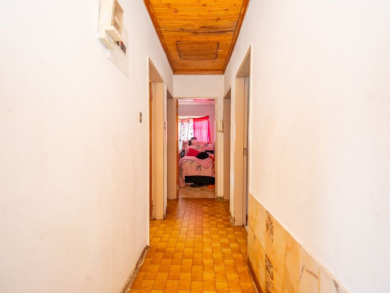 A functional hallway featuring timber ceiling paneling, tiled flooring, and partial wall tiling, providing access to adjacent rooms.