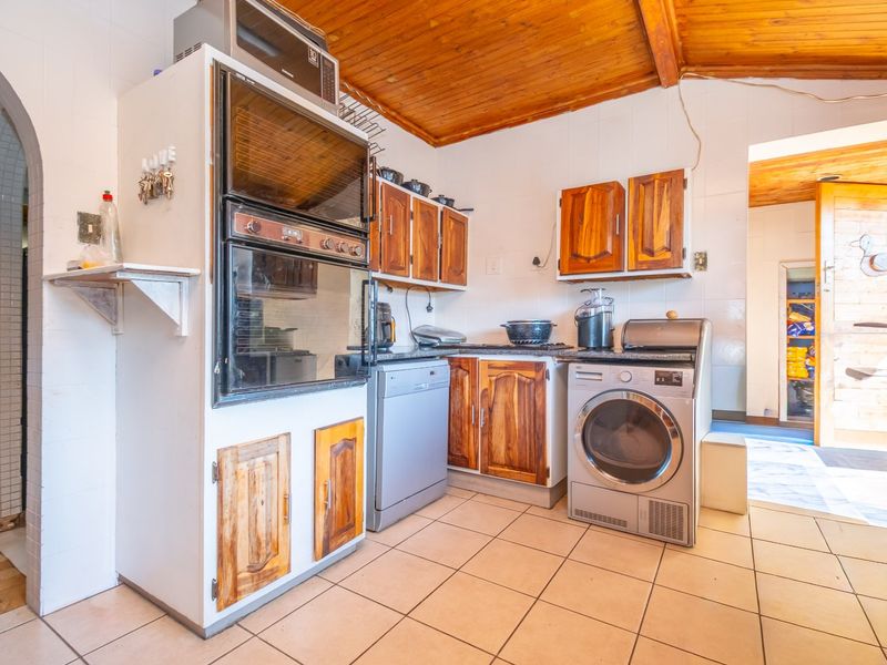 A dated kitchen featuring wooden cabinetry, tiled splashbacks, and a timber ceiling, with integrated oven and microwave units.