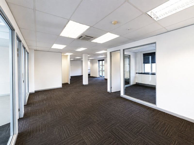 A spacious, vacant commercial office suite featuring modern glass partitioning, carpet tile flooring, and a suspended ceiling with integrated lighting and air conditioning.