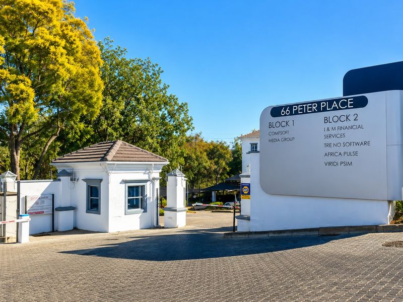 Front entrance of 66 Peter Place commercial office park, featuring a security guard house, paved driveway, and prominent business directory signage.