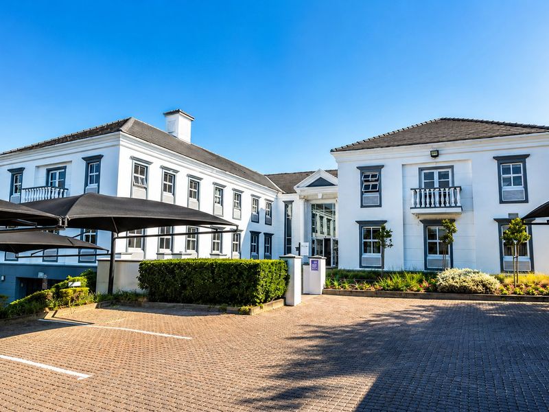 A well-maintained commercial office building featuring a paved parking area, shade sail structures, and a classic multi-story white facade with balconies.